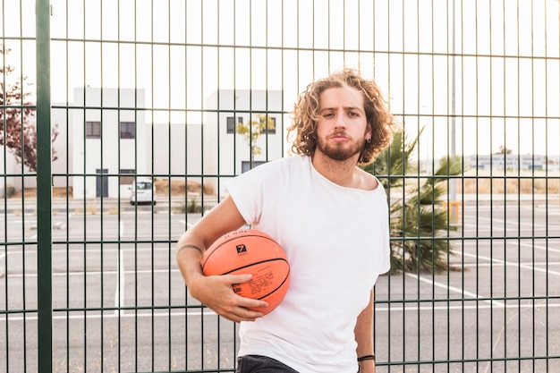 Portrait of a man holding basketball standing against fence