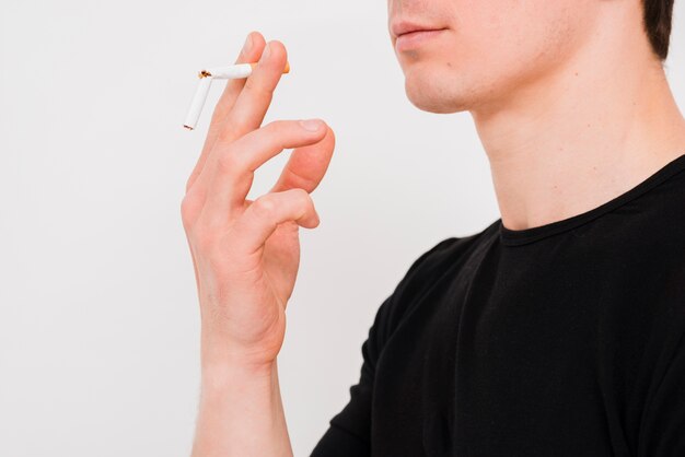 Portrait of man holding broken cigarette on white wall