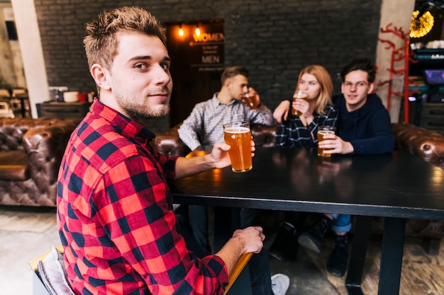 Portrait of a man holding the glass of beer sitting with friends looking at camera