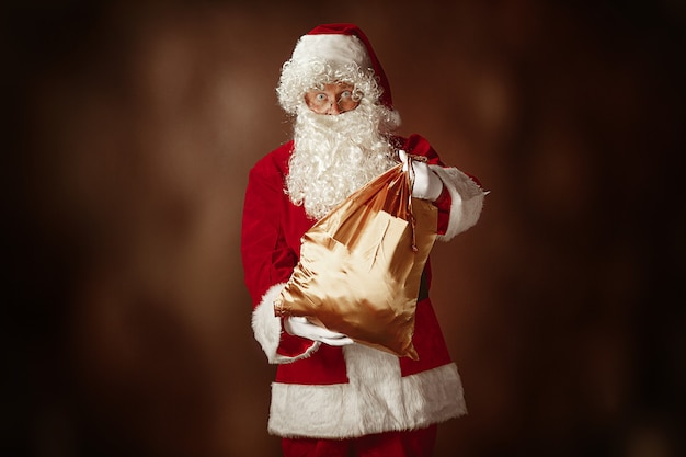 Free Photo portrait of man in santa claus costume - with a luxurious white beard, santa's hat and a red costume at red studio background with gifts