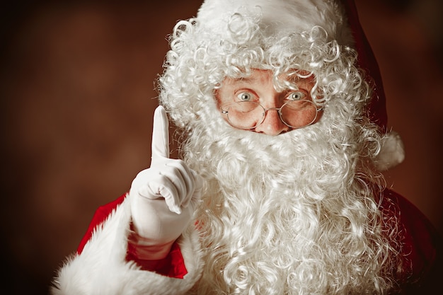 Free photo portrait of man in santa claus costume with a luxurious white beard, santa's hat and a red costume at red