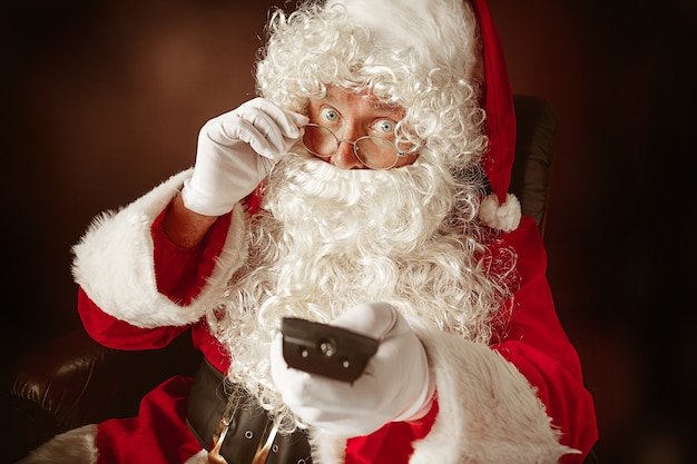 Portrait of Man in Santa Claus with a Luxurious White Beard, Santa's Hat and a Red Costume at red studio background