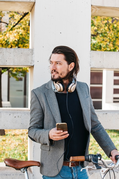 Portrait of a man standing near the wall with bicycle holding mobile phone