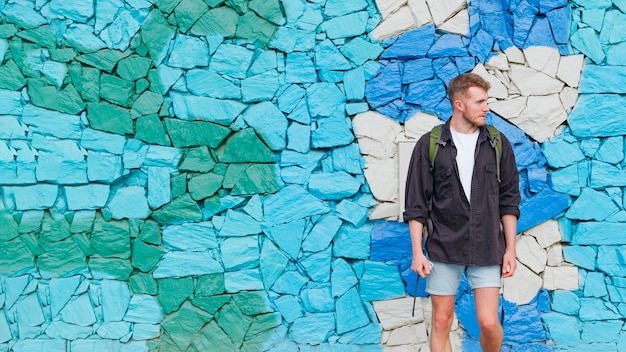 Free Photo portrait of man with backpack standing against painted stone wall