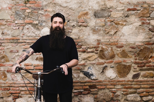 Free photo portrait of a man with bicycle standing in front of abandoned wall