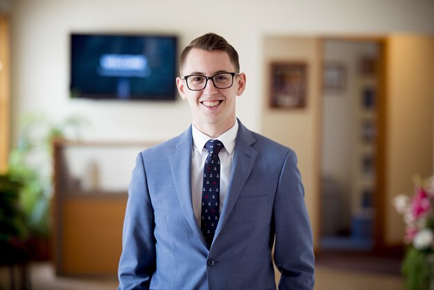 Portrait of a man with glasses in a blue suit with a tie under the lights with a blurry background