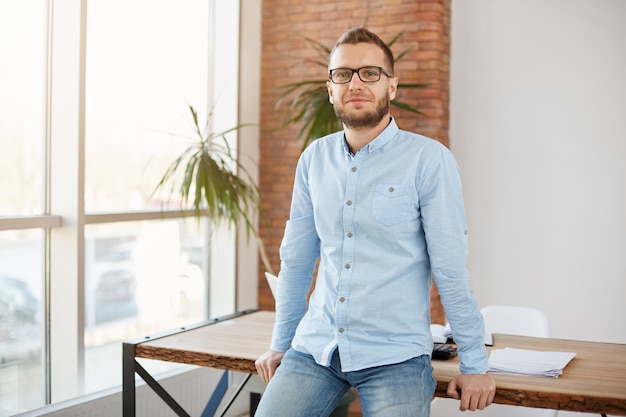 Portrait of mature male freelance designer in glasses and casual clothes, standing in modern co-working space