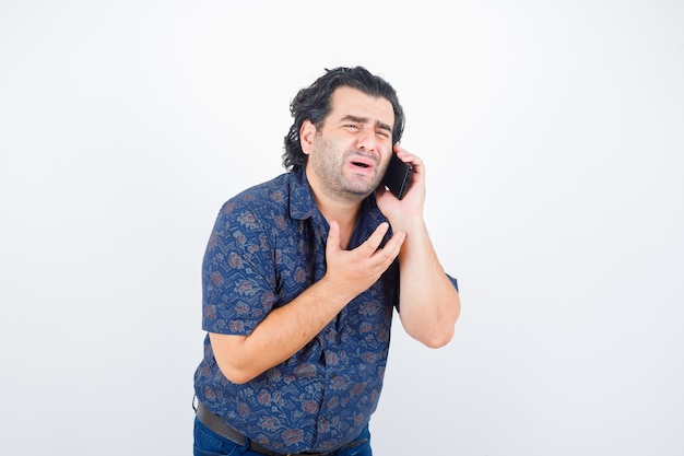 Portrait of mature man talking on mobile phone in shirt and looking wistful front view