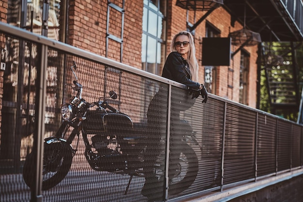 Portrait of mature sexy woman standing on the balcony next to her motorbike.