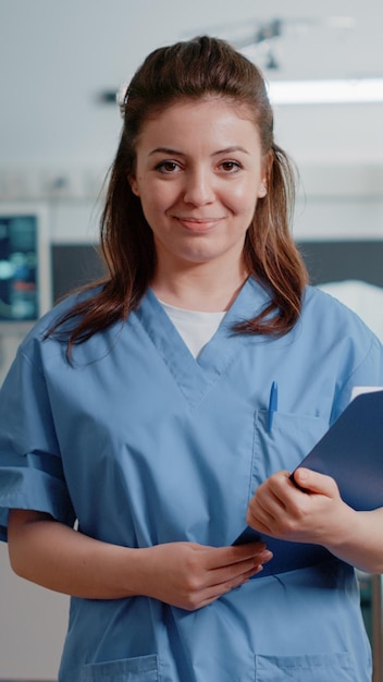 Free photo portrait of medical assistant holding checkup documents to help doctor with treatment and medicine. woman working as nurse with uniform and tools looking at camera to cure patient