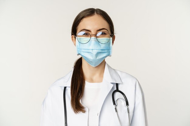 Portrait of medical worker female physician in face mask from covid during pandemic smiling and look...