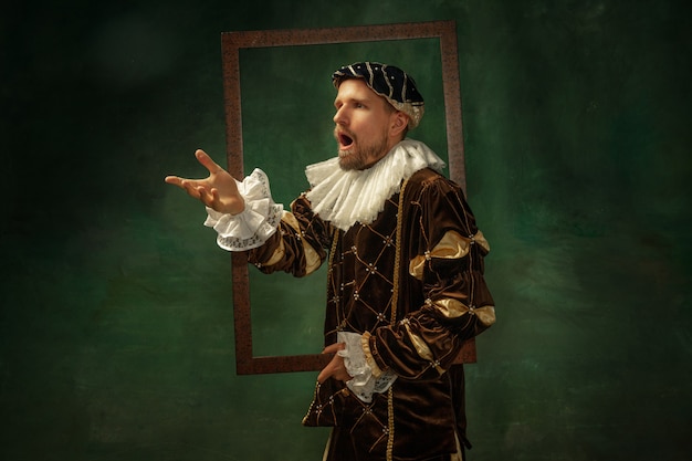 Free Photo portrait of medieval young man in vintage clothing with wooden frame on dark wall