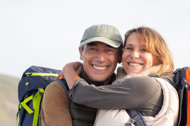 Portrait of merry elderly hikers. Man and woman with backpacks looking at camera, hugging. Hiking, family concept