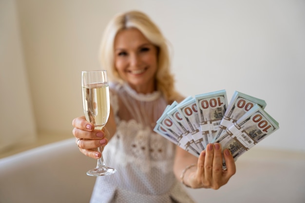 Free photo portrait of middle-aged blonde rich woman with champagne glass and banknotes