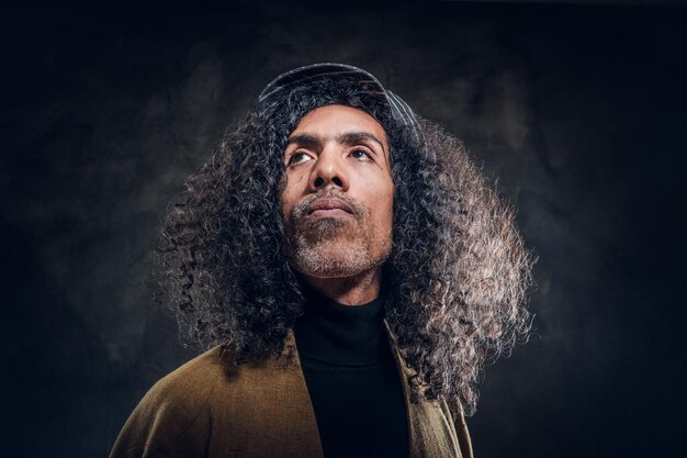 Portrait of middle aged charismatic man in brown coat at dark photo studio.