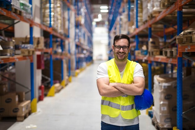 Portrait of middle aged warehouse worker standing in large warehouse distribution center with arms crossed