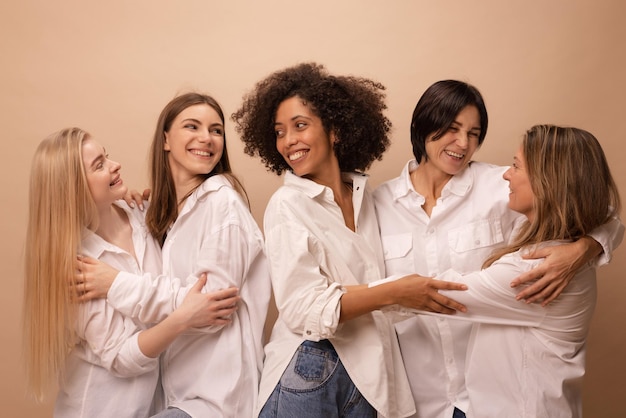 Free photo portrait of multiethnic adults and young women in white shirts hugging each other on brown background