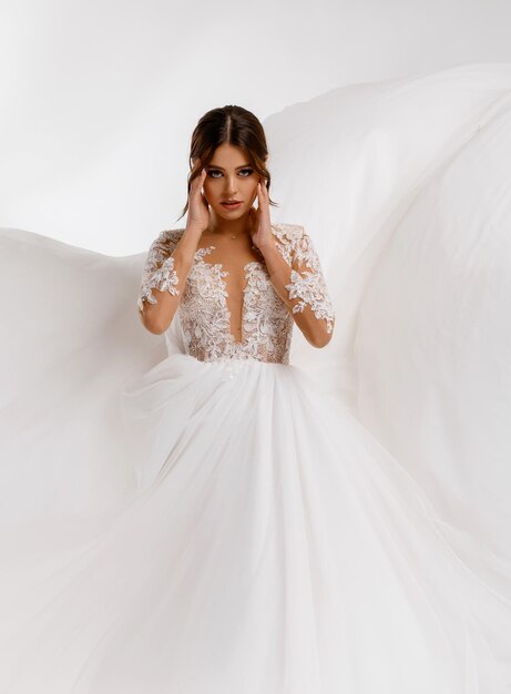 Portrait of mysterious young princess girl in wedding white puffy dress posing alone with waving wedding dress with lace on the background Adorable bride woman Wedding makeup