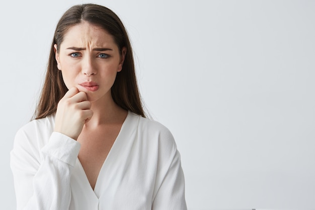 Portrait of nervous young brunette girl thinking holding hand on chin .