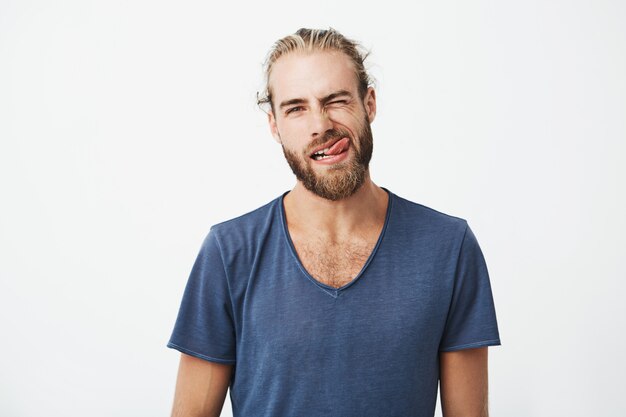 Portrait og beautiful young man with stylish hair and beard making funny and silly face