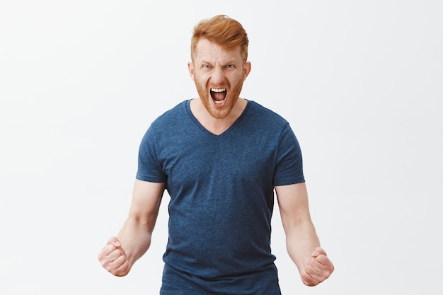 Free photo portrait of outraged angry and pissed strong masculine redhead male with bristle, clenching fists in anger, shouting, wrinkling nose, being in rage about to punch someone