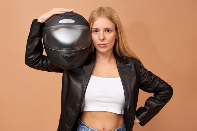 Portrait of overjoyed cheerful young female rider with teeth braces and long straight hair posing isolated in black leather jacket