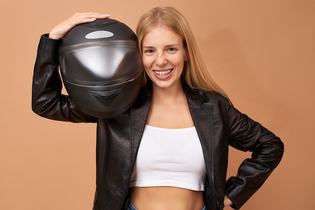 Free photo portrait of overjoyed cheerful young female rider with teeth braces and long straight hair posing isolated in black leather jacket