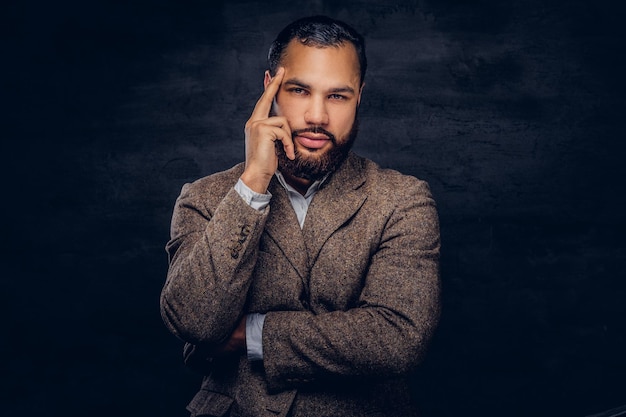 Free photo portrait of a pensive african-american man, dressed in a classic brown jacket standing in a studio on a dark background.