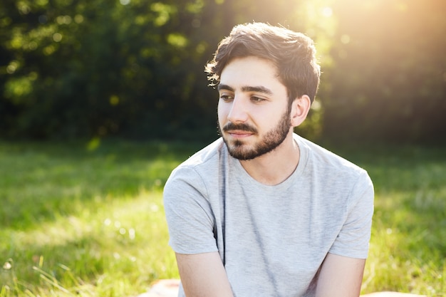 Portrait of pensive bearded male with stylish hairdo looking down with his charming big dark eyes thinking over his life enjoying stillness