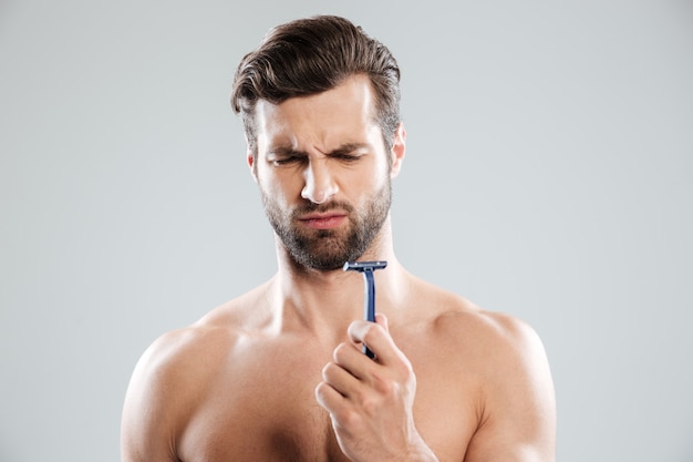 Portrait of pensive bearded naked man looking at razor