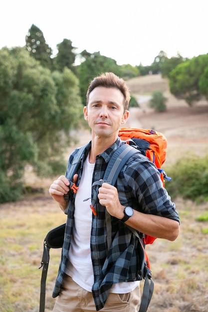 Free photo portrait of pensive male traveler standing on nature. handsome caucasian man traveling and carrying backpack. backpacking tourism, adventure and summer vacation concept