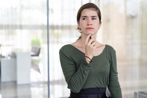 Portrait of pensive young woman standing at office wall