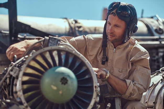 Free photo portrait of a pilot-mechanic in uniform and flying helmet, repairing the dismantled airplane turbine in an open-air museum.