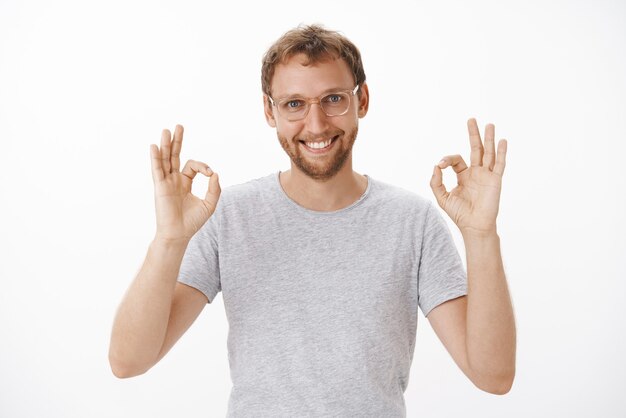 Portrait of pleased friendly and self-assured handsome bearded man in glasses raising both hands on okay or excellent gesture smiling assuring work will done in time