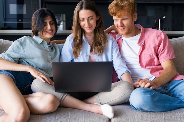 Free photo portrait of polyamorous couple at home sitting on the couch and using laptop