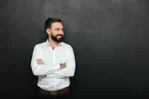 Free photo portrait of positive man in white shirt standing with arms folded, and looking away over dark gray copy space