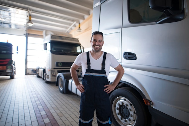 Portrait of positive smiling truck serviceman standing by truck vehicle in workshop