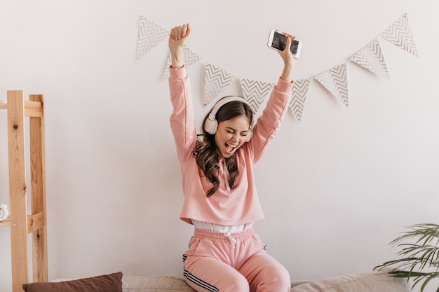 Free photo portrait of positive woman in pink sweatshirt joyfully raising hands up