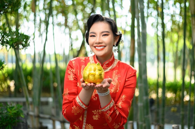 Free Photo portrait pretty asian woman in a chinese cheongsam posing with piggy bank on bamboo forest