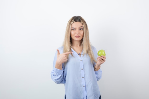 Free photo portrait of a pretty attractive woman model standing and pointing at a green fresh apple .