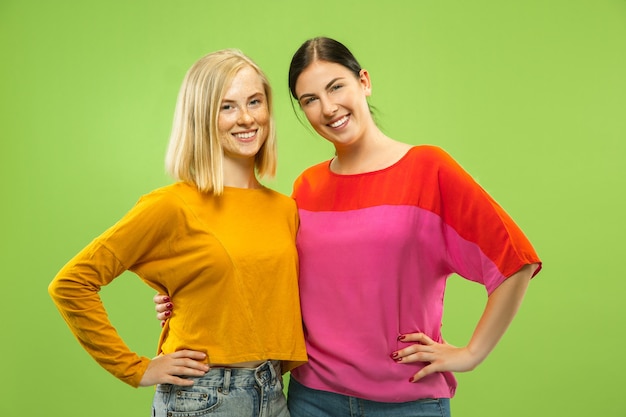 Free Photo portrait of pretty charming girls in casual outfits isolated on green studio background. two female models as a girlfriends or lesbians. concept of lgbt, equality, human emotions, love, relation.