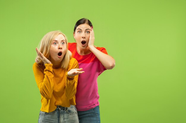 Portrait of pretty charming girls in casual outfits isolated on green studio wall