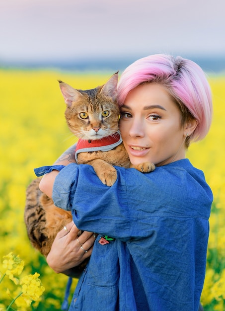 Free Photo portrait of pretty female with pink hair , resting on nature, holding cat on her arms and looking at camera