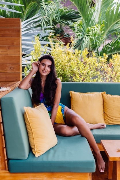 Free photo portrait of pretty fit slim positive woman resting with pillow at home on summer outdoor sofa, enjoying time alone