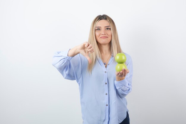 Portrait of a pretty girl model holding fresh apples and showing a thumb down.