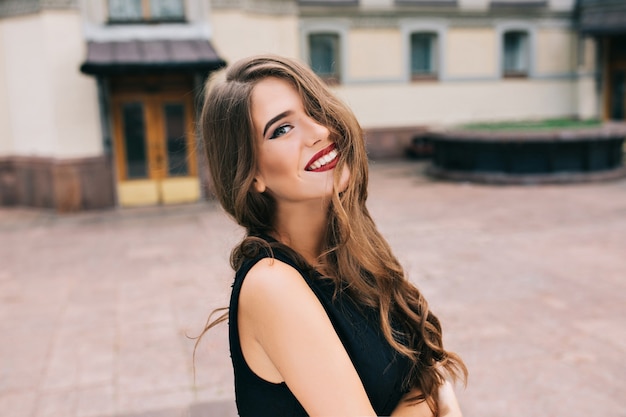 Portrait of pretty girl with long curly hair posing  on street