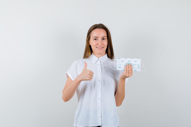 Portrait of pretty lady holding mask and showing thumbs up