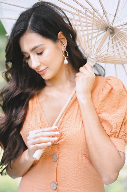 Portrait of pretty lady at nature holding umbrella in orange dress during daytime.