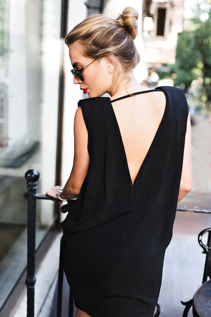 Portrait  pretty model in black dress with naked back on terrace. She is looking down.