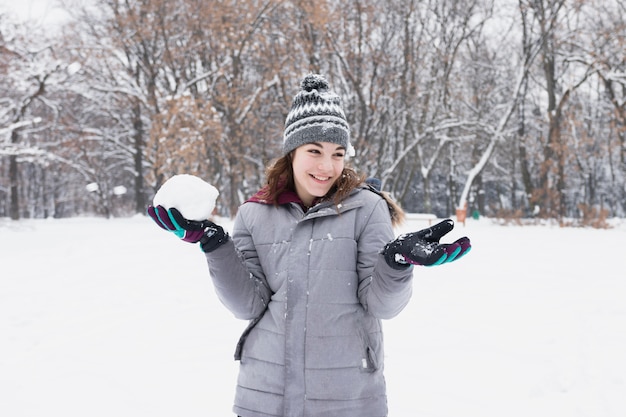 Portrait of a pretty smiling girl holding snowball at forest